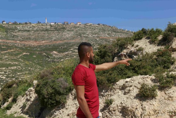 Ahmad Sabah, 21 ans, montre l'endroit où son meilleur ami, Omeir Shahada, a été tué après que des colons de Yitzhar (en arrière-plan) ont attaqué le village d'Urif (MEE/Akram al-Wara)