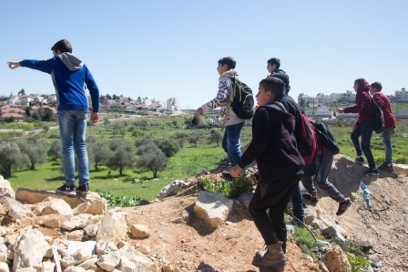 Des enfants du camp de Jalazone pistent les soldats israéliens. En fond, la colonie de Bet El ; à droite, le mur de séparation, dont une ouverture permet l'accès à une maison palestinienne (MEE/ Laurent Perpigna Iban)