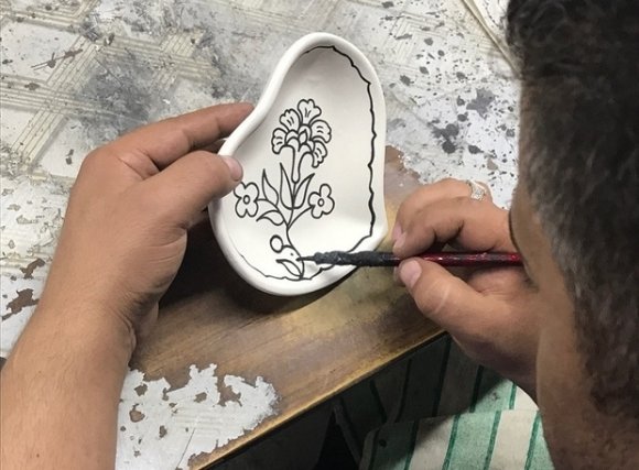 Un artisan dessine un motif floral sur une coupelle en céramique (MEE/Katie Miranda)