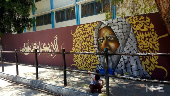 Un garçon s'accroupit devant une des peintures de Talaa sur un mur de la ville de Gaza (Baraa Khaled/MEE)